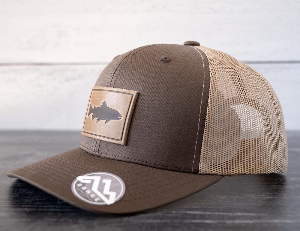 Right angled view of the RANGE Leather Trout hat in the color brown & khaki against a white and black rustic wood background