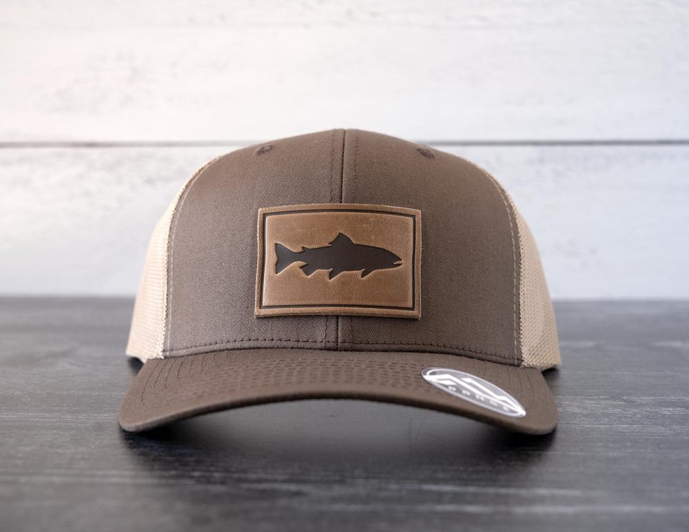 Front view of the RANGE Leather Trout hat in the color brown & khaki against a white and black rustic wood background