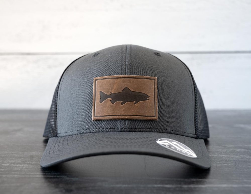 Front view of the RANGE Leather Trout hat in the color charcoal against a white and black rustic wood background
