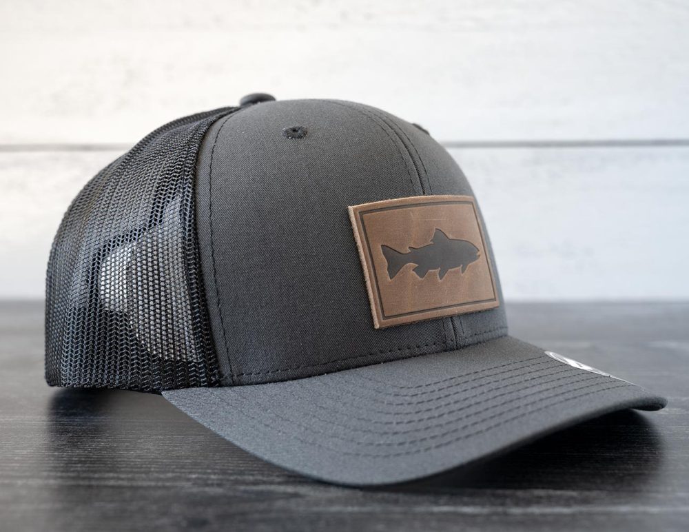 Left angled view of the RANGE Leather Trout hat in the color charcoal against a white and black rustic wood background