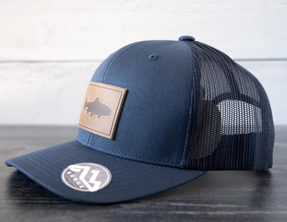 Right angled view of the RANGE Leather Trout hat in the color navy against a white and black rustic wood background
