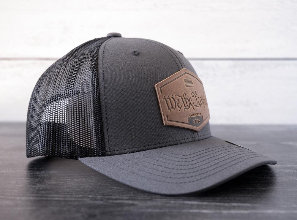 Left Angled view of the RANGE Leather We the People hat in the color charcoal against a white and black rustic wood background