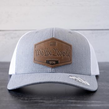 Front view of the RANGE Leather We the People hat in the color heather gray & white against a white and black rustic wood background