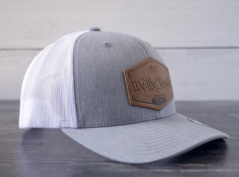 Left angled view of the RANGE Leather We the People hat in the color heather gray & white against a white and black rustic wood background