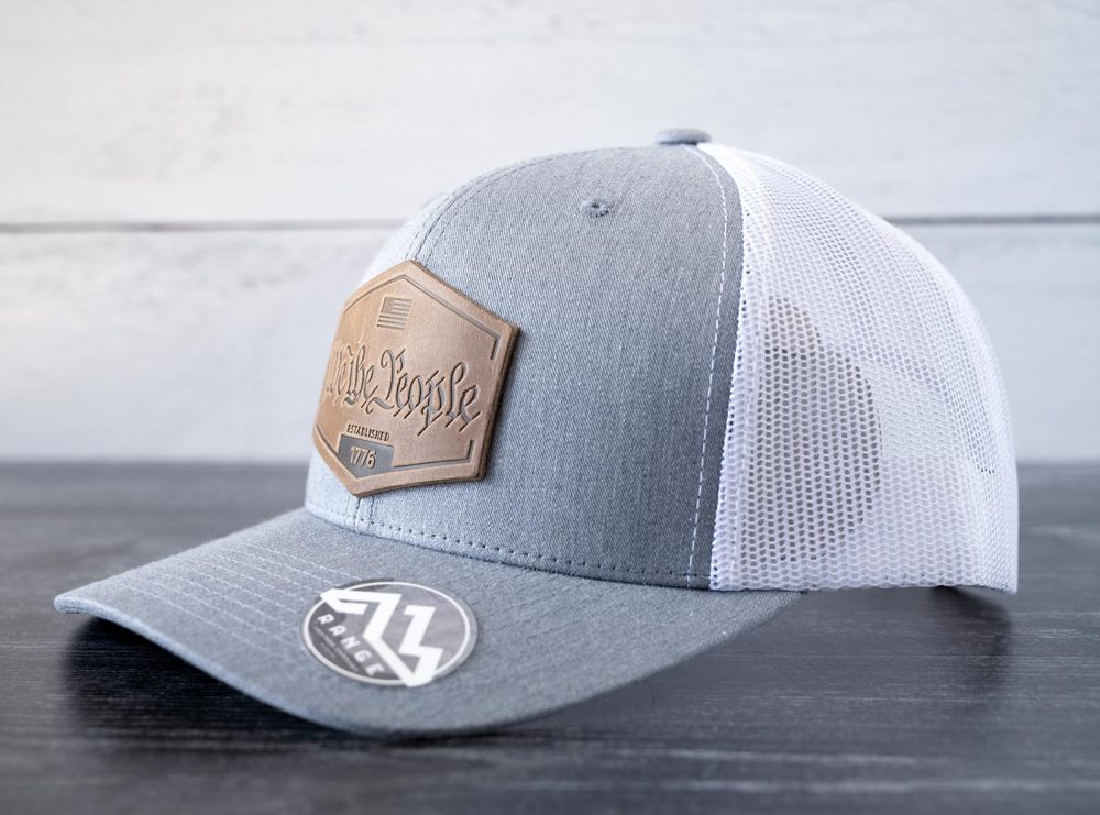 Right angled view of the RANGE Leather We the People hat in the color heather gray & white against a white and black rustic wood background