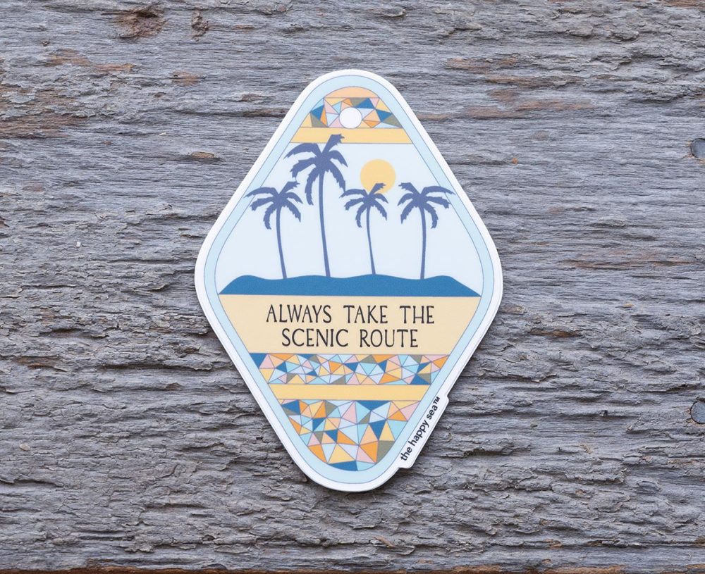 Top view of the Happy Sea Always Take the Scenic Route sticker on a rustic wood background