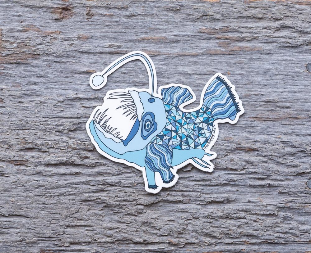 Top view of the Happy Sea Anglerfish sticker on a rustic wood background